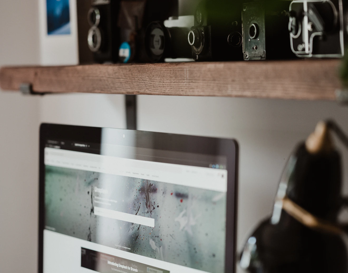 Biurko freelancera z monitorem i kolekcją aparatów na drewnianej półce