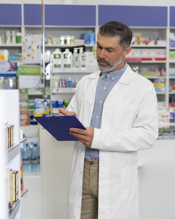 Farmaceuta z podkładką notuje przy regałach z lekami