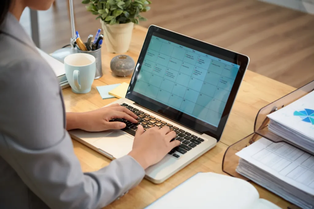 Kobieta pracuje przy laptopie, obok leżą segregatory z dokumentami